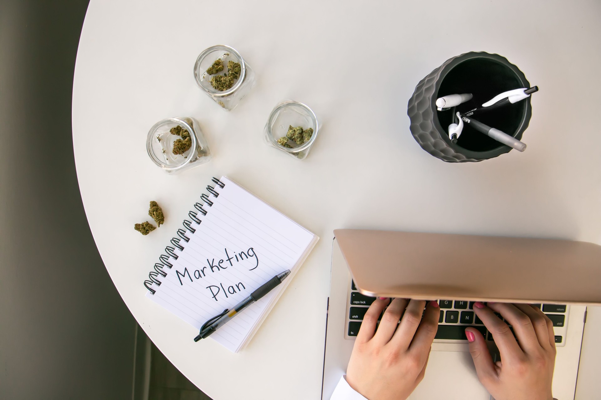 Top Down View of Cannabis Entrepreneur working on Marketing for Marijuana Business on White Table Work Space